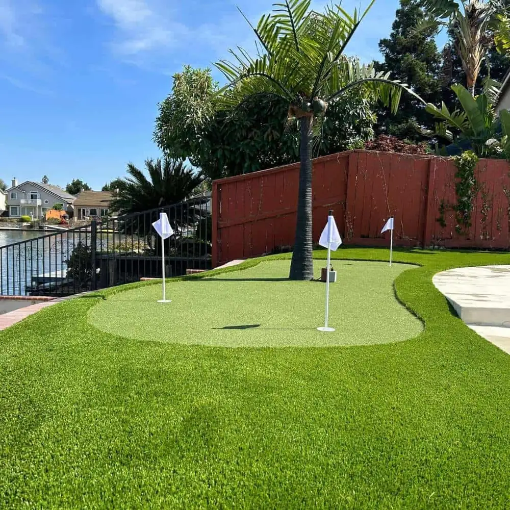 Backyard synthetic turf putting green with golf flags beside a lakeside outdoor entertaining area