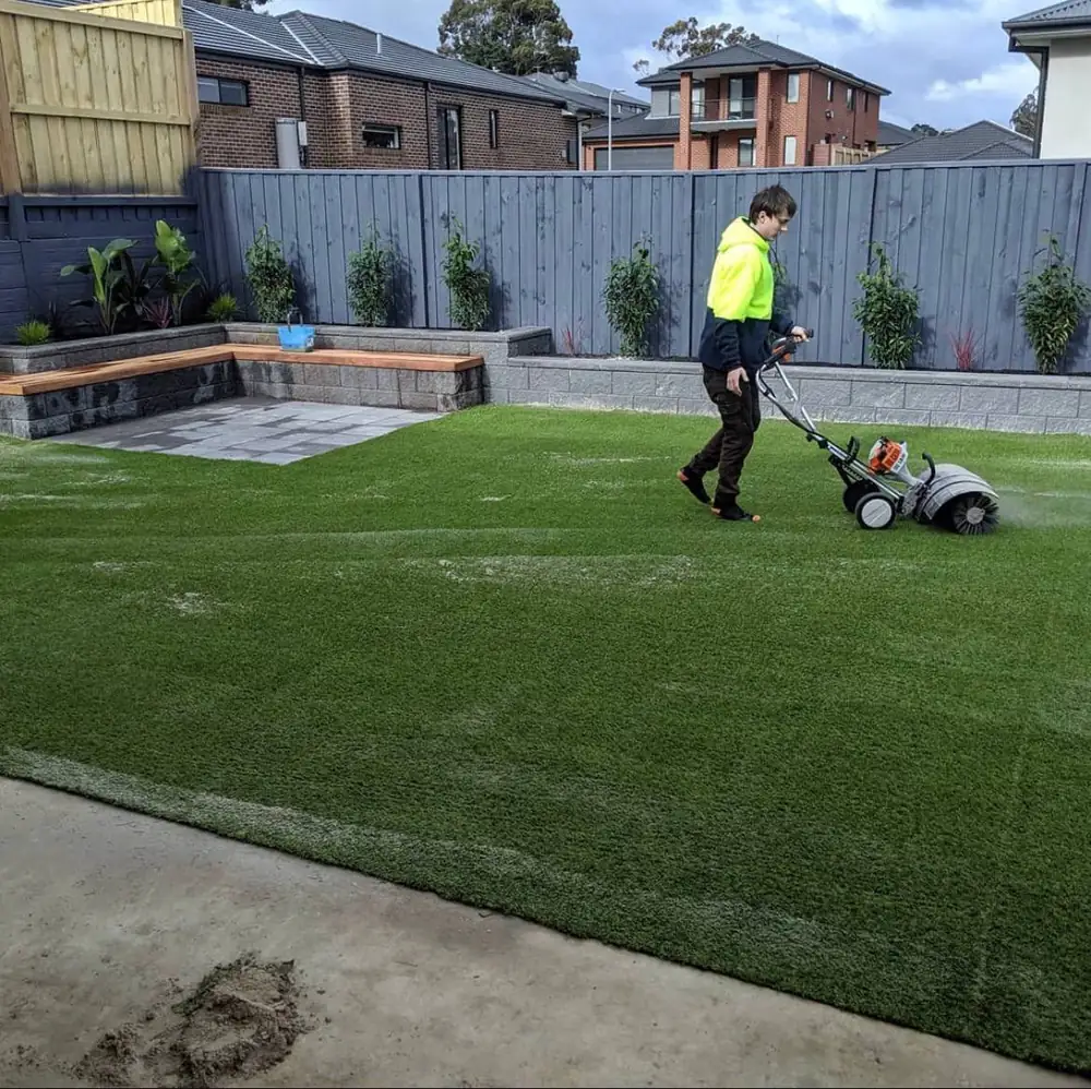 Synthetic turf installation in a Melbourne backyard with professional worker using brushing equipment